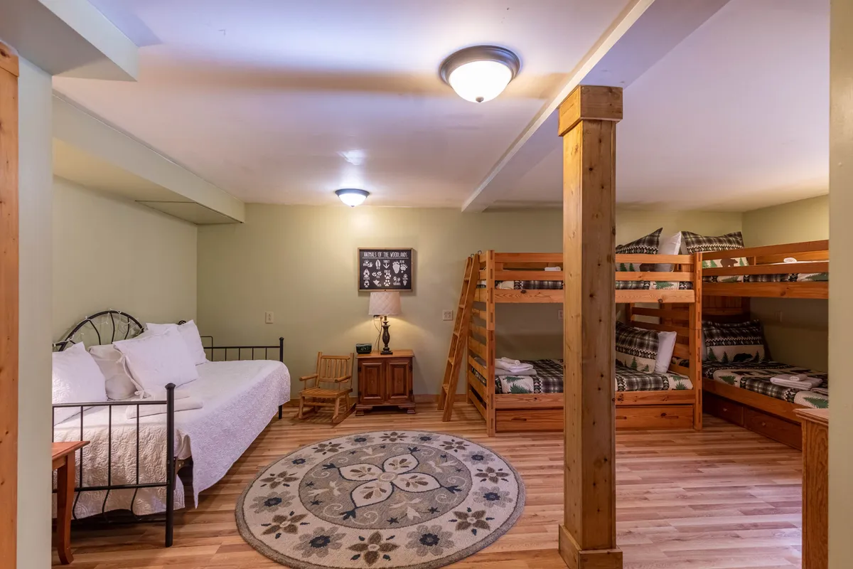 A family-friendly bunk room with twin-over-twin bunks, a daybed, a decorative rug, and wooden furniture. The space is bright and inviting, ideal for kids or groups to relax, play games, or enjoy a good night's sleep.