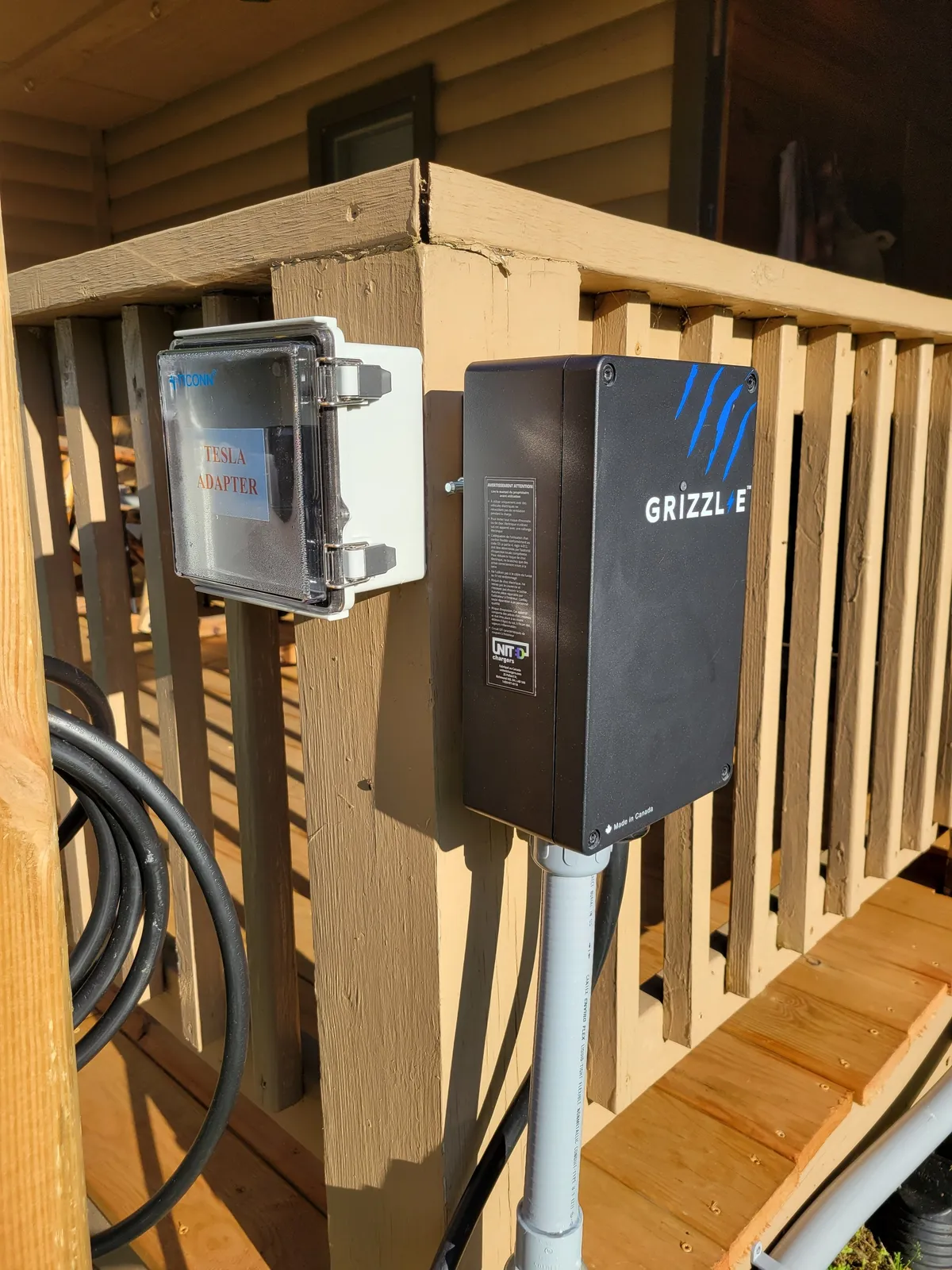 A close-up view of a wooden deck equipped with an electric vehicle charger, wooden railing, and ample space for outdoor gatherings. The scene emphasizes eco-friendliness and the convenience of outdoor living, with the deck opening up to the surrounding natural landscape.