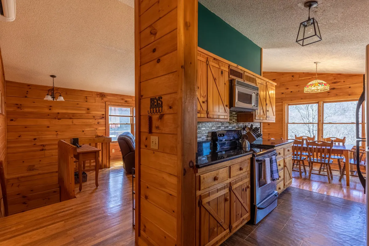 A warm, inviting kitchen with wooden cabinetry and stainless steel appliances, seamlessly connected to a dining area with a large window. The stained glass light fixture above the dining table adds character, while the spacious countertops suggest a well-equipped space ideal for preparing family meals.