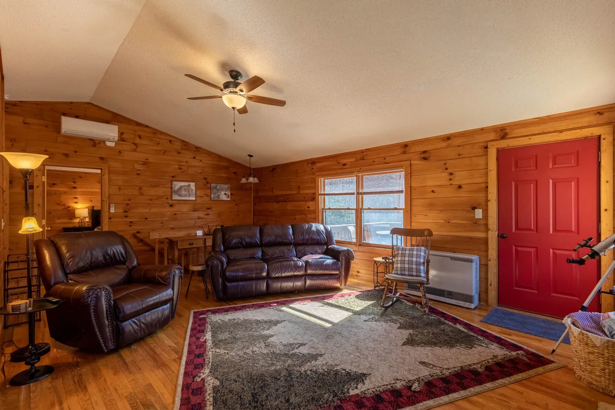 A view of the welcoming entryway and living space, with leather sofas, a bold red door, wood-paneled walls, and a patterned area rug. The cozy setup invites guests to step in, relax, and make themselves at home, creating an immediate sense of welcome and warmth.