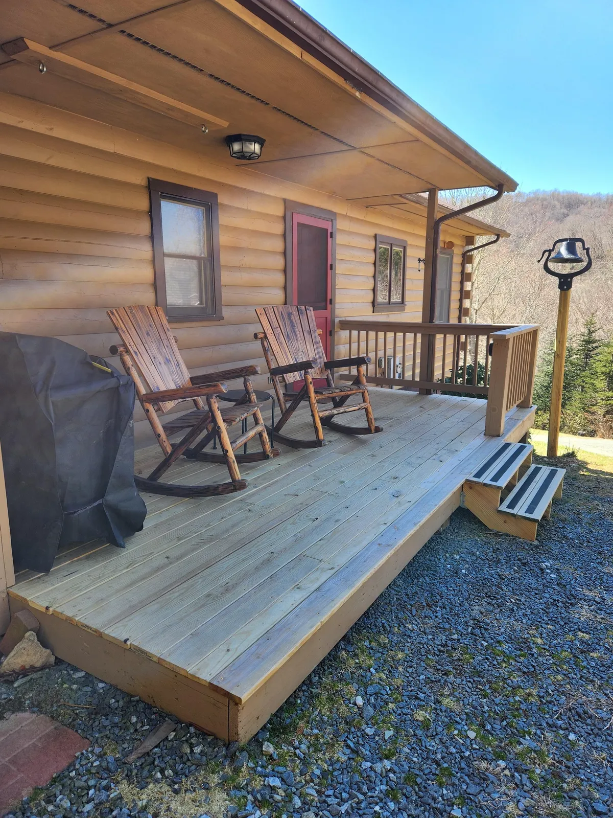 The image shows rocking chairs on a deck with an inviting entryway and expansive landscape views. The scene captures a restful ambiance ideal for reading, relaxing, or simply soaking in the natural beauty.
