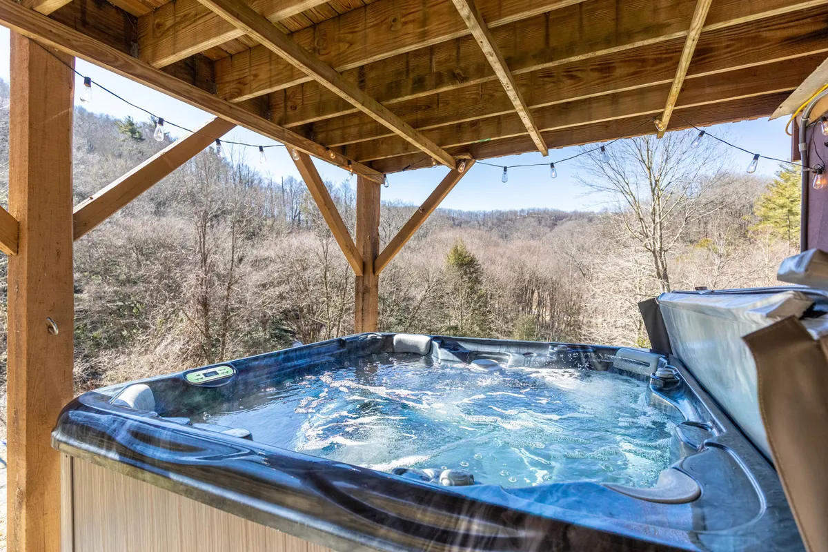 An exterior view of the private hot tub nestled on a wooden deck, surrounded by scenic views. The setting is tranquil and designed for relaxation, with space for six people to unwind under the stars or take in nature.