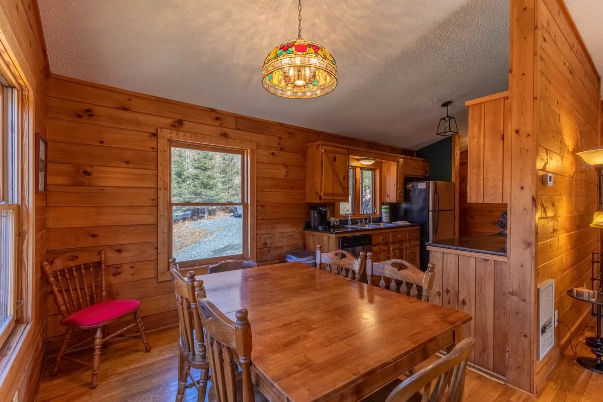 A homey dining area with a wooden table, stained glass light fixture, and a window offering an inviting glimpse outdoors. The scene suggests gatherings, shared meals, and moments of togetherness against a rustic, mountain backdrop.