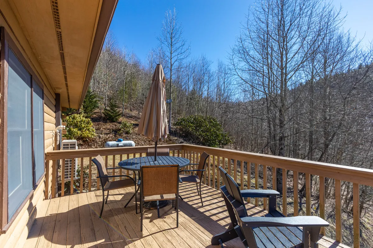 A peaceful wooden deck set amidst trees, featuring a round table with an umbrella and chairs, perfect for outdoor dining or relaxing. The setting is surrounded by greenery, providing a tranquil yet accessible atmosphere.